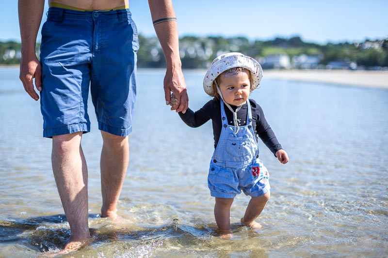 enfant tient la main de son papa et marche dans la mer
