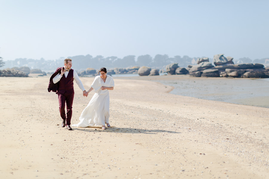 mariés qui marchent mains dans la main sur la plage de st Anne a Tregastel