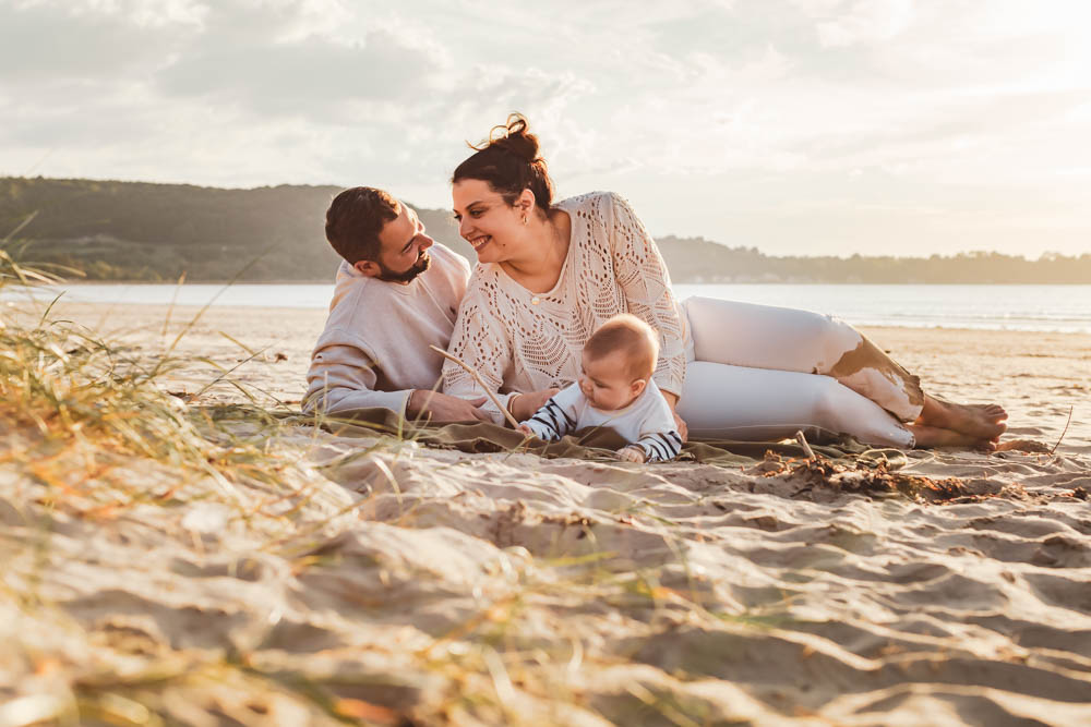 parent heureux avec bebe a la plage allongé dans le sable