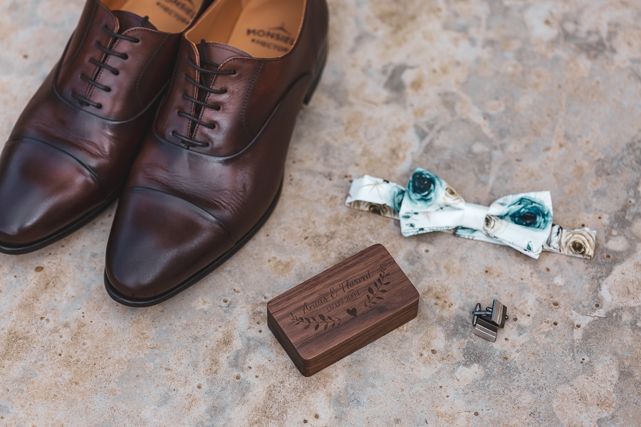ecrin en bois personnalisé des alliances, avec les boutons de manchettes, le noeud papillon et les chaussures en cuir du marié sur le béton