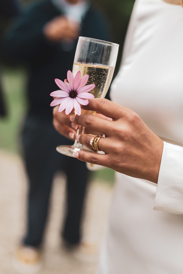 la mariée tient une fleur avec sa coupe de champagne et son alliance