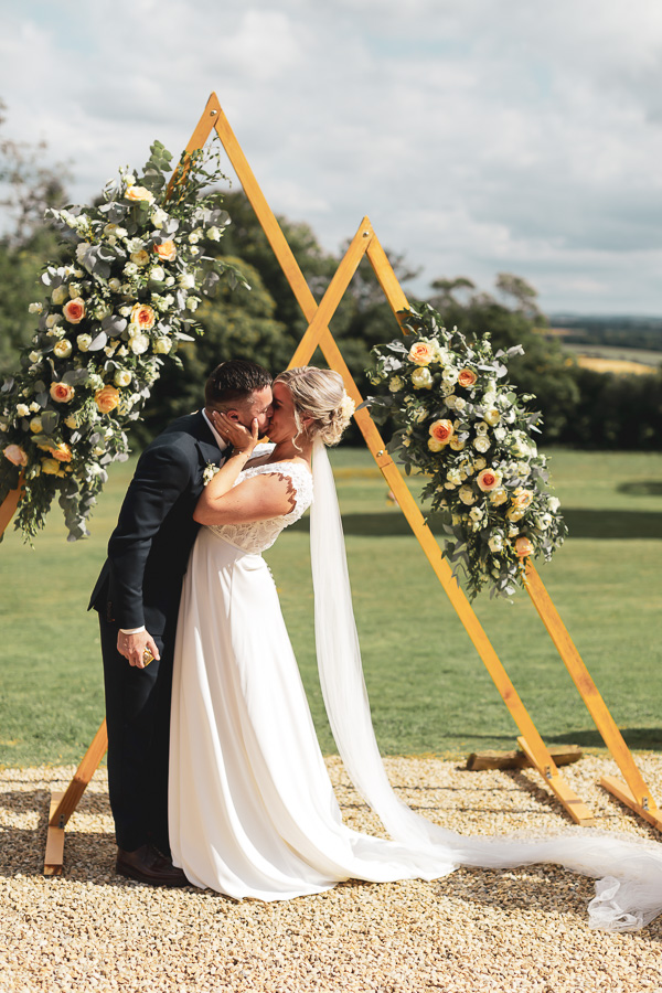 les mariés qui s'embrassent a la fin de la cérémonie laique devant l'arche fleurie