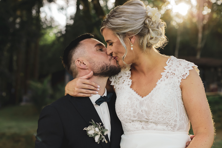 Les mariés qui s’embrassent dans les jardins de Kerezellec avec le soleil du soir qui filtre à travers les arbres