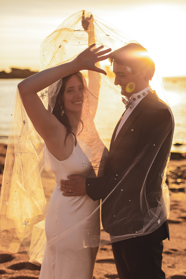 Les mariés face à face sous le voile de la mariée au coucher du soleil sur la plage de l'ile Renote