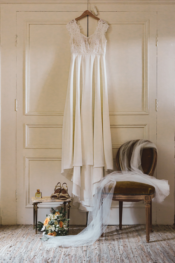 photo de la robe de la mariée, de son voile et accessoires davant une vieille armoire et un siege vintage