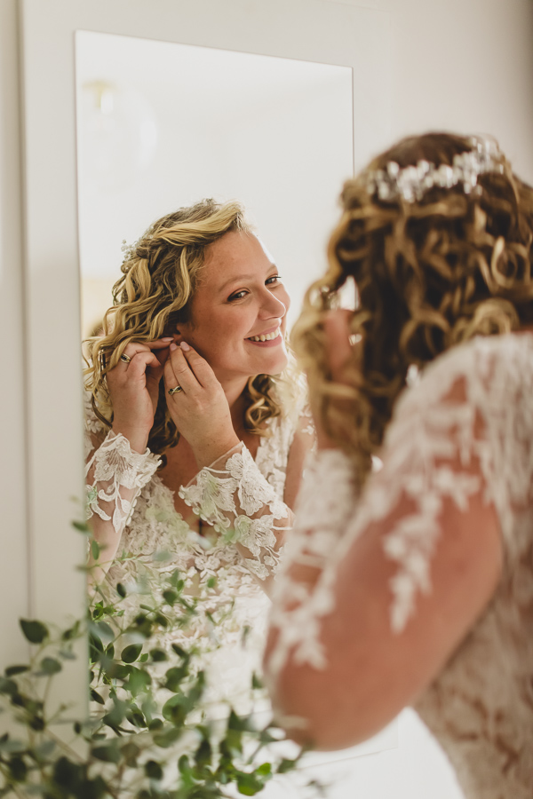 reflets de la mariée dans un miroir mettant ses boucles d'oreilles