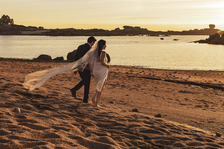 Les mariés marchent ensemble main dans la main au coucher du soleil sur la plage de l'ile Renote