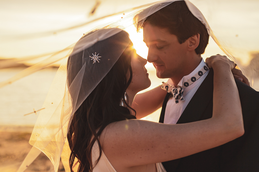Les mariés face à face sous le voile de la mariée au coucher du soleil sur la plage de l'ile Renote