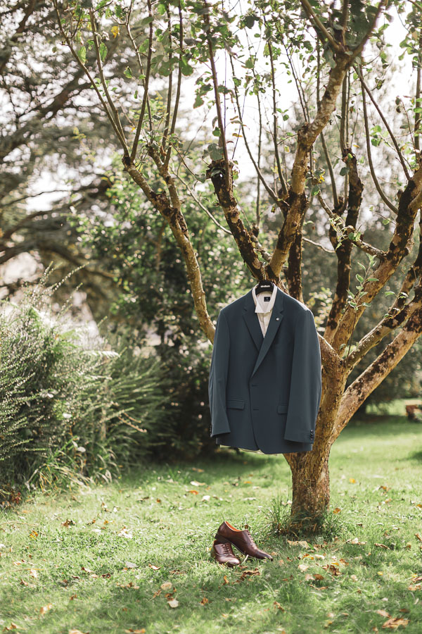 photo de la veste du costume accroché à un arbres, dans les tons vert émeraude, avec ses chaussures
