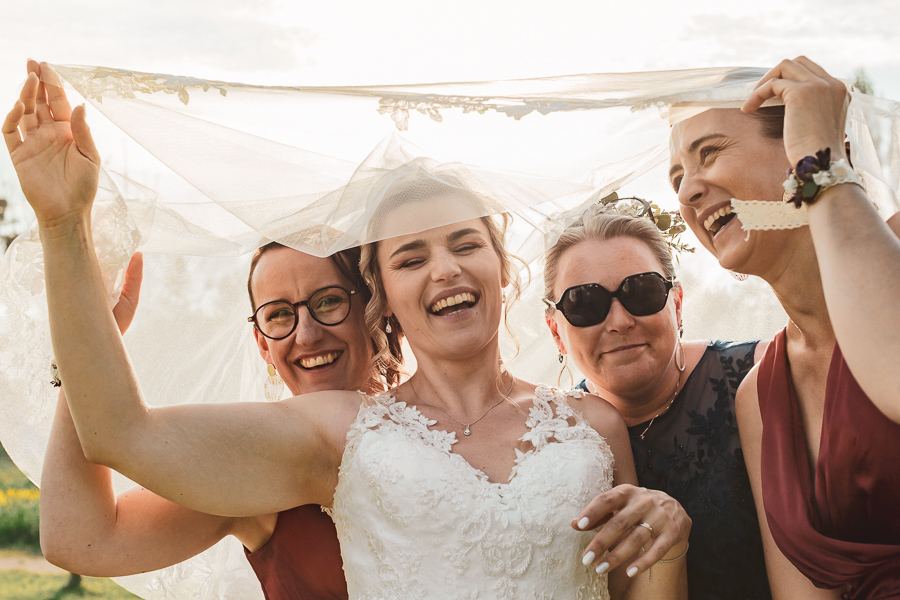 la mariée et ses témoins s'amusent sous le voile de la mariée