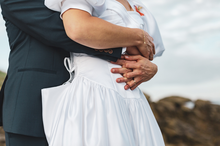 Photo des mains d'un couple de mariés enlacés où l'on voit les alliances