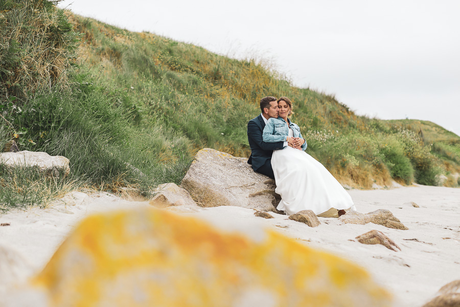 Les mariés enlacés et assis sur un rocher à la plage pour les photos de couple. Romantique et intime