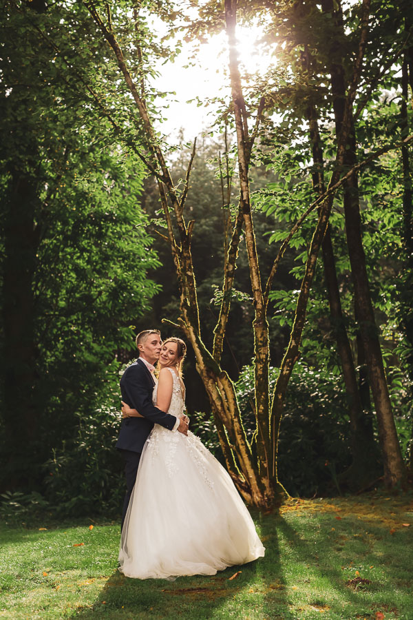 mariés enlacés et amoureux dans la lumière qui filtre à travers les arbres