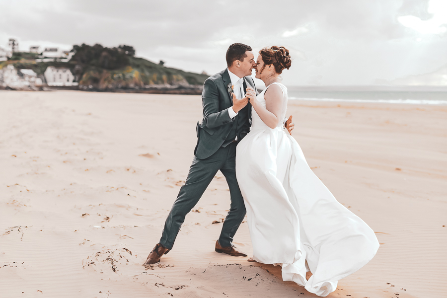 Les mariés dansent sur la plage de Pléneuf Val André avec élégance et la robe de la mariée vole dans le vent.