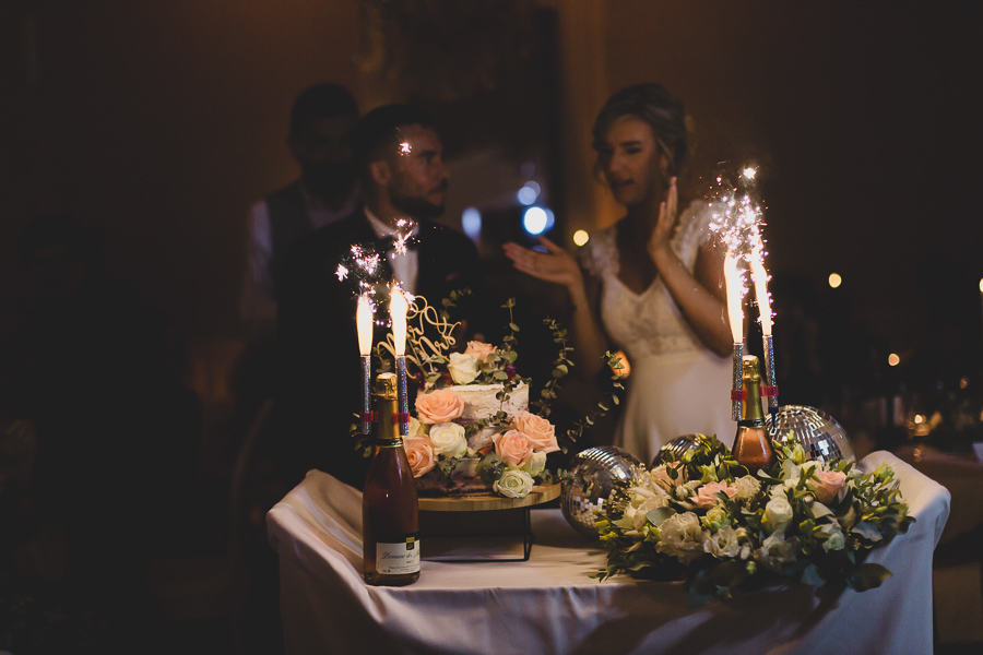 Les mariés présentent le gâteau décoré avec des fleurs et avec des cierges magiques.