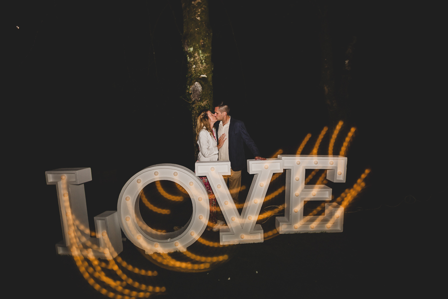 Couple amoureux dans la nuit qui s'embrassent devant le mot LOVE lumineux