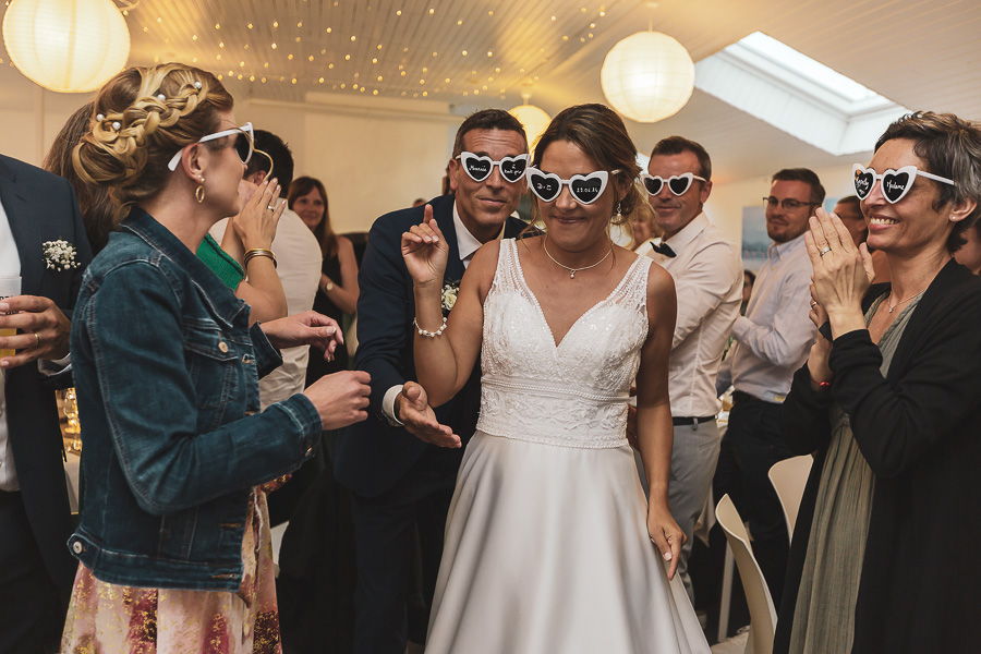 Entrée des mariés dans la salle de reception avec des lunettes de soleil blanches fun en forme de coeur. Les Terrasses de l'Aber
