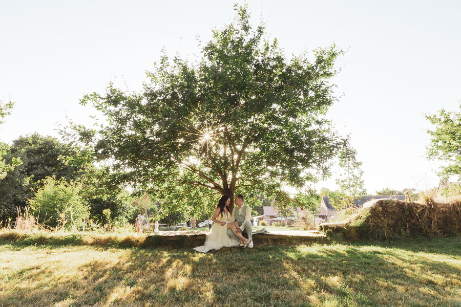 Les mariés assis sous un chêne avec le soleil qui brille à travers les branches