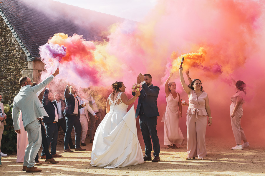 couple de mariés dans les fumigènes orange et rose dans la cour du manoir de Kerellou