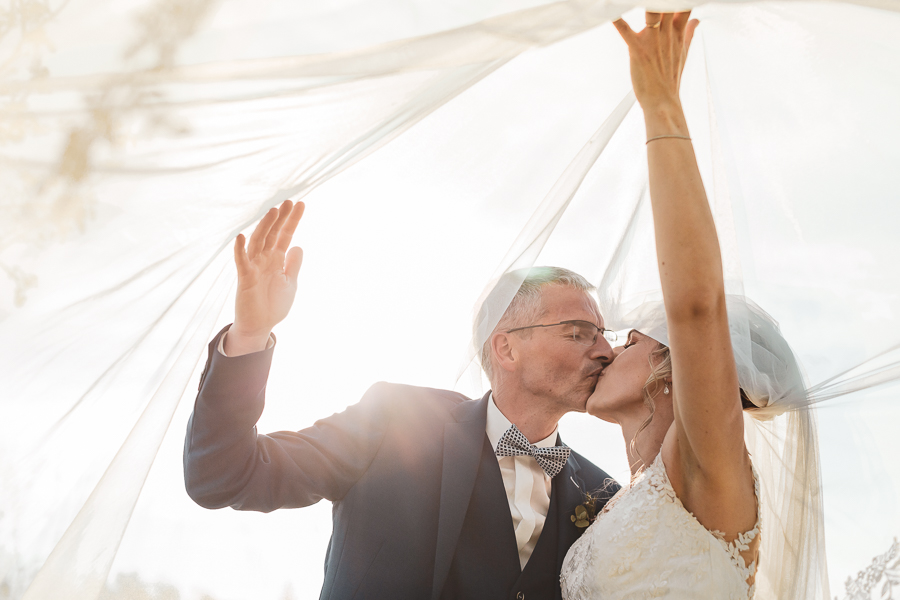 Les mariés s'embrassent sous le voile de la mariée et le soleil brille à travers