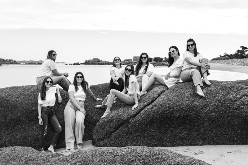 les filles et la futures mariée assises dans les rochers à la plage sur la cote de granit rose pour une photos de groupe chic et moderne