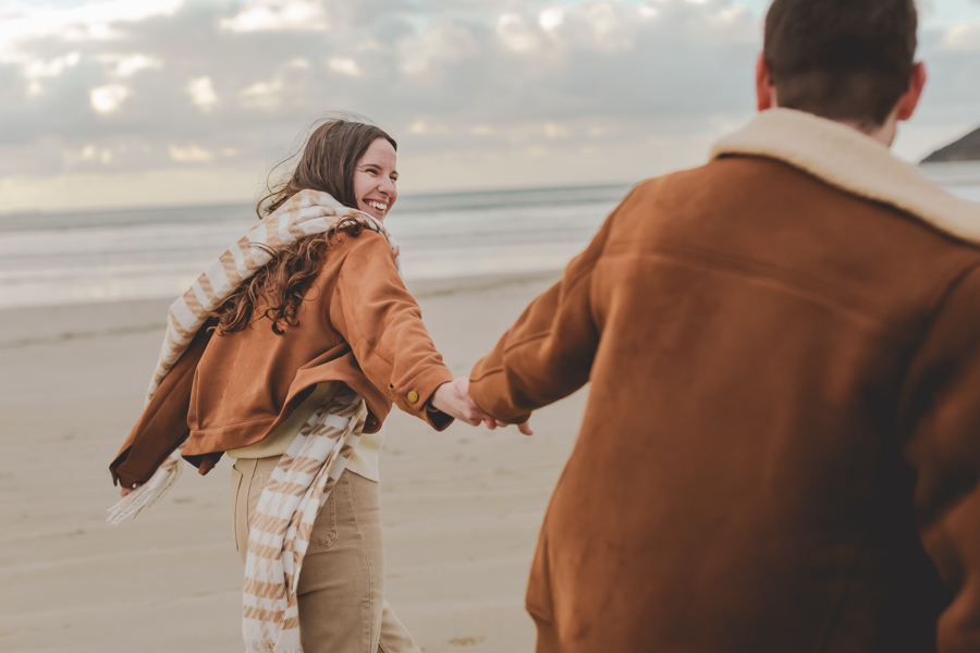 couple complice se tient par la main a la plage pendant la seance photo