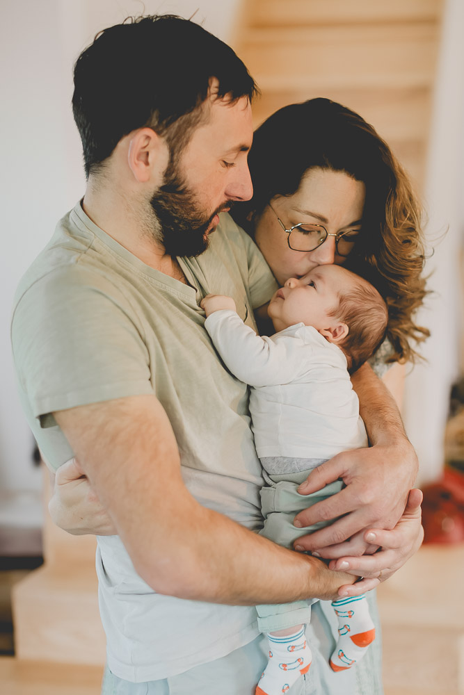 bebe dans les bras de papa et maman fait un bisous moment de tendresse
