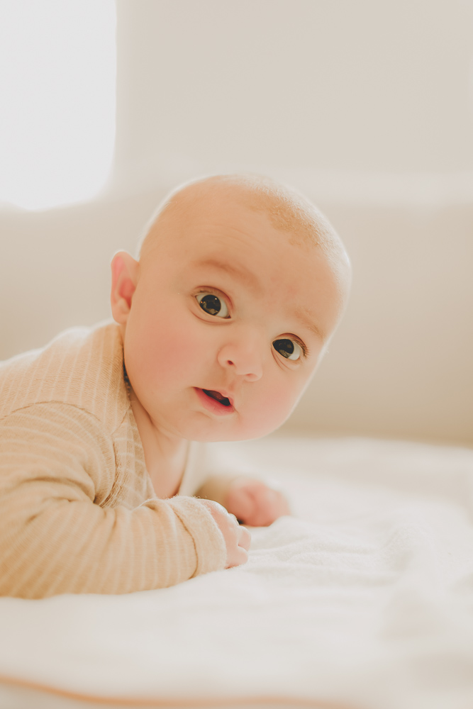 bébé sur le ventre qui se dresse avec un regard rigolo